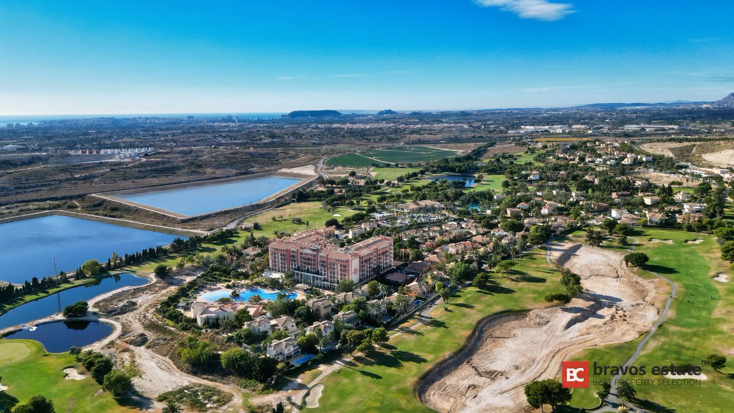 Aerial view of Bonalba Green within Bonalba Golf Resort, showing the hotel, resort pool, golf fairways, lakes, and distant Mediterranean coastline.